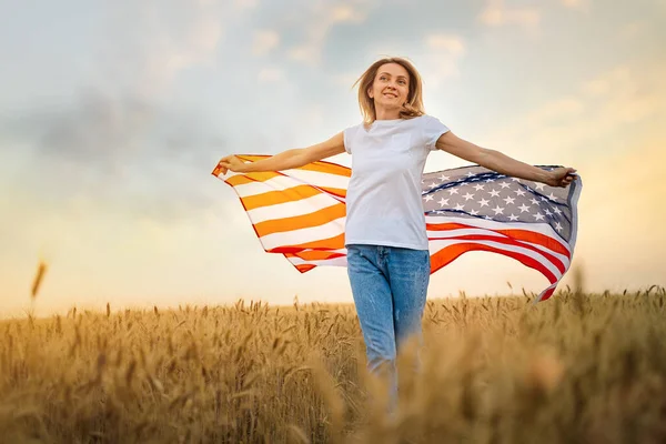 Žena běží a skákání bezstarostné s otevřenou náručí přes pšeničné pole Holding USA vlajka — Stock fotografie