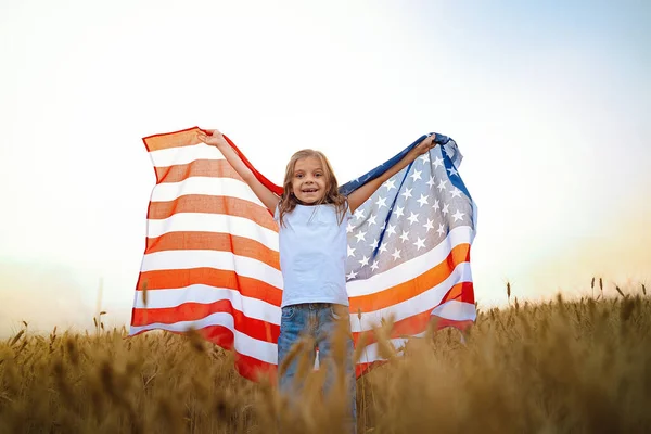 Förtjusande patriotisk flicka klädd i en amerikansk flagga på ett vackert vetefält — Stockfoto