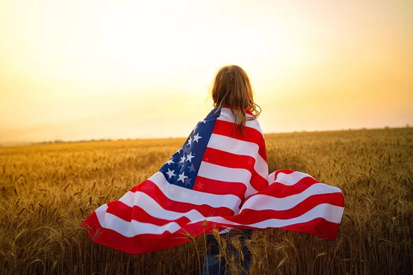 Förtjusande patriotisk flicka klädd i en amerikansk flagga på ett vackert vetefält — Stockfoto