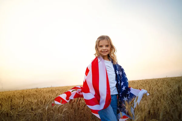 Rozkošná vlastenecká dívka s americkou vlajkou v krásném pšeničném poli — Stock fotografie