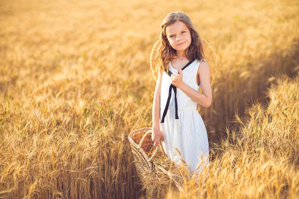 Fashion photo of a little girl in white dress and straw hat at the evening wheat field — Stock Photo, Image