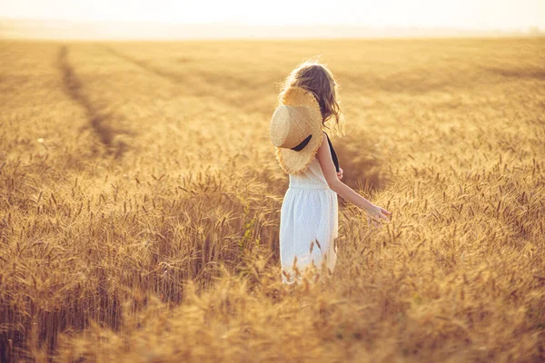 Foto di moda di una bambina in abito bianco e cappello di paglia al campo di grano di sera — Foto Stock