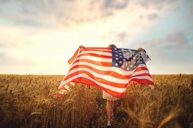 Beyaz elbiseli bir kızın, güzel bir buğday tarlasında koşarken Amerikan bayrağı taktığı arka plan görüntüsü.