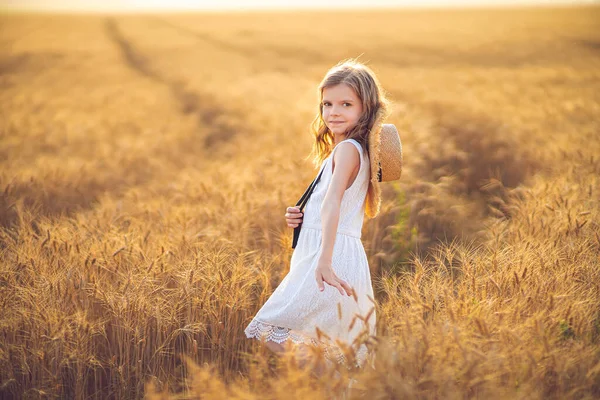 Fashion foto van een klein meisje in witte jurk en stro hoed op de avond tarweveld — Stockfoto