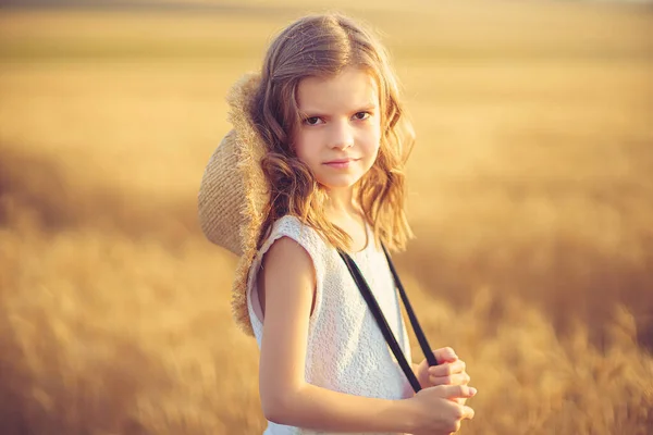 Mode foto av en liten flicka i vit klänning och halm hatt på kvällen vetefält — Stockfoto