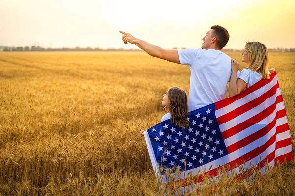 Visão traseira de uma família feliz irreconhecível no campo de trigo com EUA, bandeira americana — Fotografia de Stock