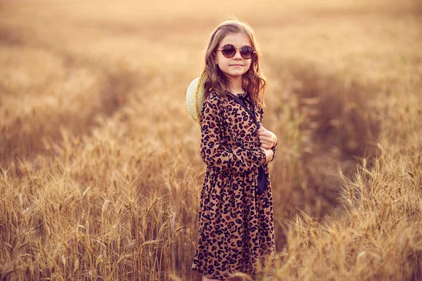 Foto de moda de uma menina em vestido de impressão de leopardo, óculos de sol e chapéu de palha no campo de trigo da noite — Fotografia de Stock