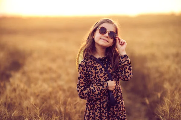 Leopar desenli elbiseli, güneş gözlüklü ve hasır şapkalı küçük bir kızın moda fotoğrafı. — Stok fotoğraf