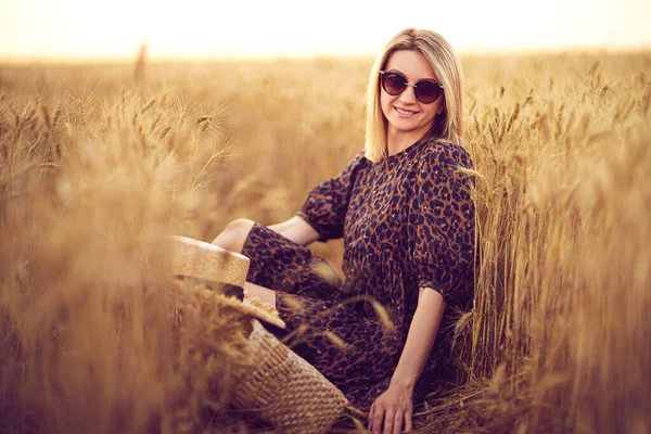 woman in animal print dress, straw hat in front of Sun in middle of wheat field with pleasure , enjoying summer holidays