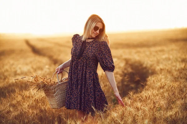 Mujer en vestido de animal print, sombrero de paja delante del sol en medio del campo de trigo con placer, disfrutando de las vacaciones de verano — Foto de Stock