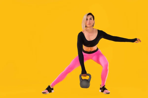 穿着时髦的粉色和黑色运动服的健身女人穿着黄色背景的水壶进行锻炼. — 图库照片