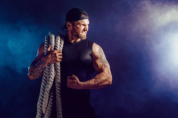 Brodaty atletyczny wyglądający kulturysta trzymający linę bojową na ciemnym tle studia z dymem. Siła i motywacja — Zdjęcie stockowe