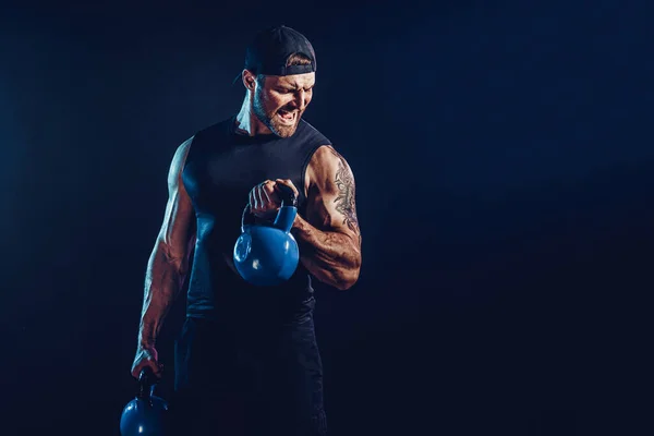 Aggressive bearded muscular bodybuilder doing Exercise for the shoulder muscles, deltoid with kettlebell.