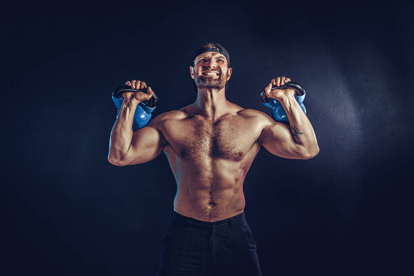 Aggressive bearded muscular bodybuilder doing Exercise for the shoulder muscles, deltoid with kettlebell.