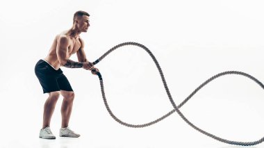 Çekici kaslı adam ağır iplerle çalışıyor. Beyaz arka planda izole edilmiş spor giysili yakışıklı bir adamın fotoğrafı.