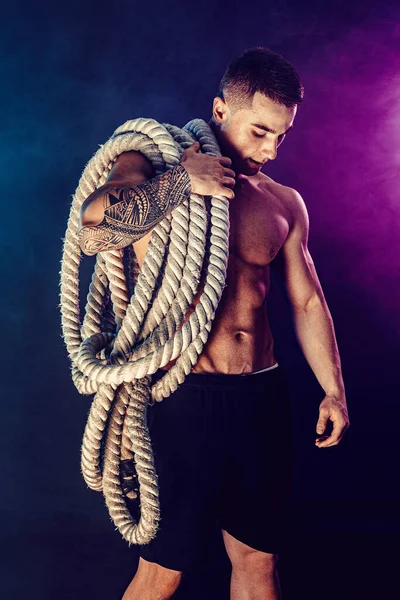Bearded athletic looking bodybulder holding battle rope on dark studio background with smoke. Strength and motivation — Stock Photo, Image