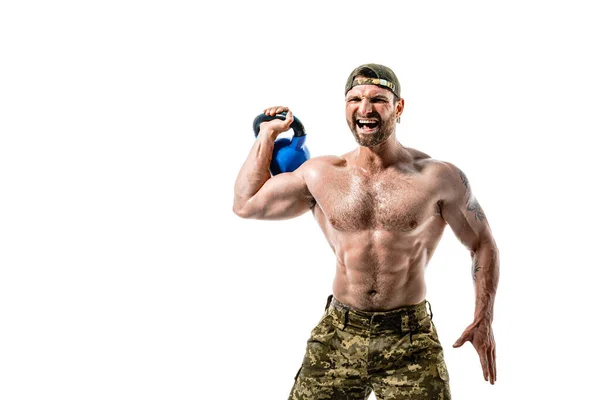 Muskulös idrottare bodybuilder man i camouflage byxor med en naken bål träning med kettlebell på en vit bakgrund. — Stockfoto