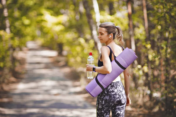 Woman in sport clothes holding a yoga mat and water bottle after workout