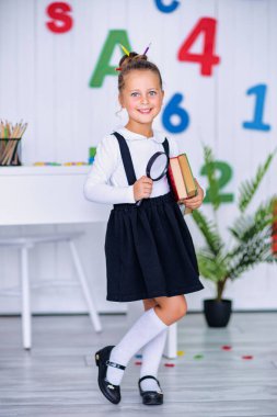 Masadaki mutlu gülümseyen öğrenci. Sınıftaki çocuk kalemlerle, kitaplarla. İlkokuldan bir çocuk. Sonbaharın ilk günü. Okula geri dön.