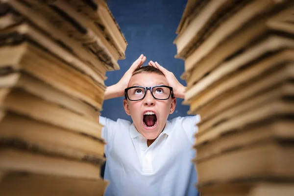 Kleiner Junge im Stress verrückt beim Lernen und Hausaufgaben machen im Kinderbildungskonzept zwischen zwei Bücherstapeln sitzend. — Stockfoto