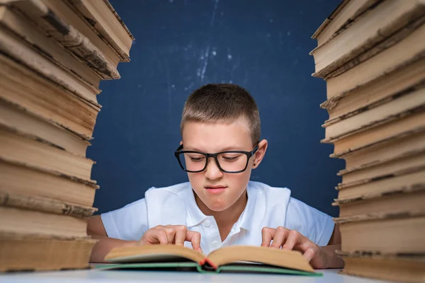 頭のいい男の子で眼鏡の間に座って二つの山の本と読書本を思慮深く — ストック写真