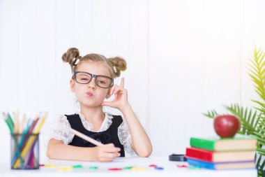 Masada gülümseyen mutlu bir öğrenci var. Sınıftaki kız kalemlerle, kitaplarla. İlkokuldan bir çocuk. Sonbaharın ilk günü. Okula geri dön.