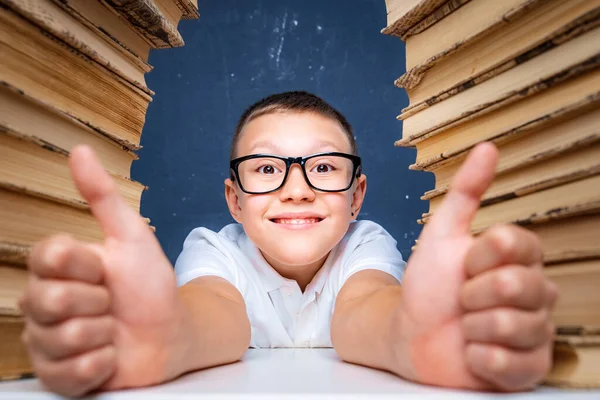 Kluger Junge mit Brille sitzt zwischen zwei Bücherstapeln und blickt nachdenklich auf — Stockfoto