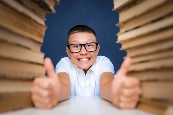 Kluger Junge mit Brille sitzt zwischen zwei Bücherstapeln und blickt nachdenklich auf — Stockfoto