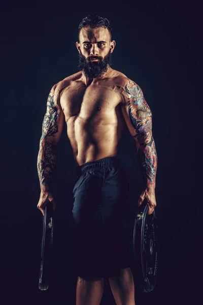 Estudio retrato de sin camisa tatuado barbudo macho sostiene mancuerna sobre fondo negro — Foto de Stock