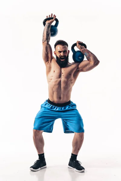 Μυώδης shirtless τατουάζ γενειοφόρος αθλητής bodybuilder προπόνηση με kettlebell σε λευκό φόντο. — Φωτογραφία Αρχείου