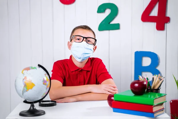 En skolpojke i medikal mask vid ett skrivbord — Stockfoto
