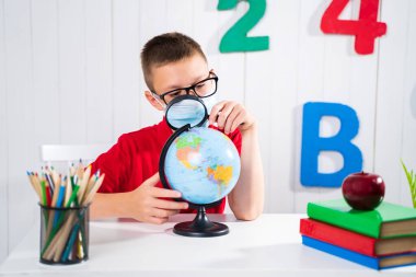 Mutlu sevimli akıllı çocuk bir masada oturuyor ve elini kaldırıyor. Çocuk arkaplanda bir tahtayla cevap vermeye hazır. Okul için hazırım. Okula dönelim. Elma ve kitaplar masanın üstünde.