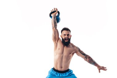 Kaslı, üstsüz, sakallı erkek sporcu. Beyaz arka planda kettlebell ile antrenman yapıyor..