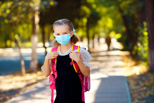 Flicka bär mask och ryggsäck skydda och säkerhet från coronavirus. Barnet går i skolan efter pandemin. Titta på kameran eleverna är redo för nytt läsår — Stockfoto