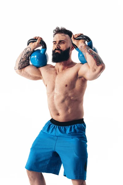 Muscolare senza maglietta tatuato atleta barbuto maschio allenamento culturista con kettlebell su uno sfondo bianco. — Foto Stock