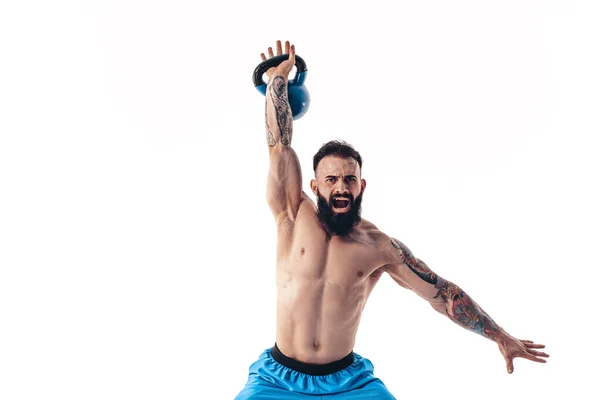 Muscolare senza maglietta tatuato atleta barbuto maschio allenamento culturista con kettlebell su uno sfondo bianco. — Foto Stock