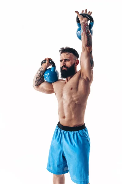 Muscular sem camisa tatuado atleta masculino musculoso atleta barbudo treino com kettlebell em um fundo branco. — Fotografia de Stock