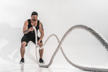 Çekici kaslı adam ağır iplerle çalışıyor. Beyaz arka planda izole edilmiş spor giysili yakışıklı bir adamın fotoğrafı.