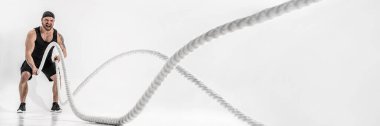 Çekici kaslı adam ağır iplerle çalışıyor. Beyaz arka planda izole edilmiş spor giysili yakışıklı bir adamın fotoğrafı.
