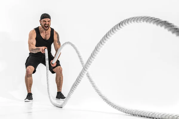 Uomo muscoloso dall'aspetto atletico barbuto che si allena con corde pesanti. Foto di bell'uomo in abbigliamento sportivo isolato su sfondo bianco. Crossfit — Foto Stock