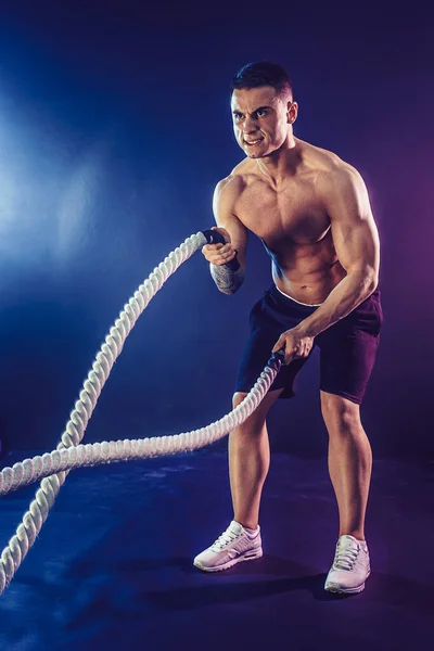 Athletic looking bodybulder work out with battle rope on dark studio background with smoke. Strength and motivation — Stock Photo, Image