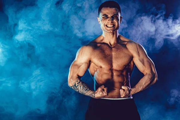 Atletisk man böjande muskler i studio på mörk bakgrund med rök. Stark bodybuilder med perfekta abs — Stockfoto