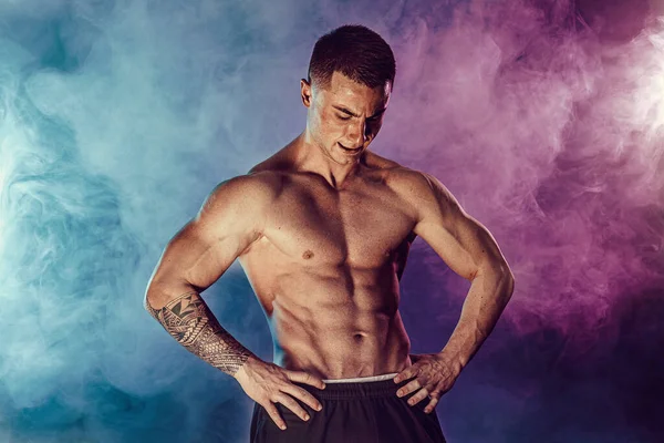 Homme sportif flexion des muscles en studio sur fond sombre avec de la fumée. bodybuilder fort avec abdos parfaits — Photo