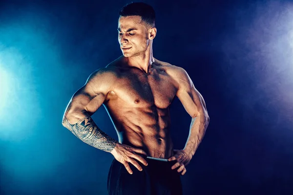 Atletisk man böjande muskler i studio på mörk bakgrund med rök. Stark bodybuilder med perfekta abs — Stockfoto