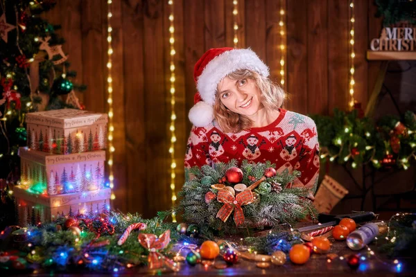 Donna che fa a mano ghirlanda di Natale sul tavolo. Decorazione e composizione natalizia. Ragazza vestita con maglione di design natalizio preparare ghirlanda di Natale per le vacanze — Foto Stock