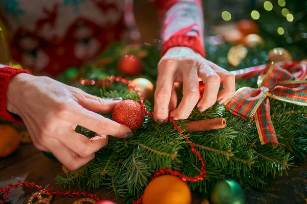 Primer plano de una mujer manos haciendo la corona de Navidad hecha a mano en la mesa para las vacaciones. Decoración y composición navideñas —  Fotos de Stock