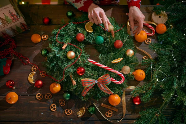 Primer plano de una mujer manos haciendo la corona de Navidad hecha a mano en la mesa para las vacaciones. Decoración y composición navideñas —  Fotos de Stock