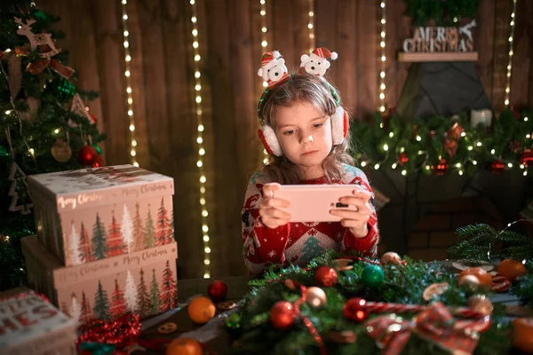 Дівчина використовує телефон біля ялинки в декоративному інтер'єрі. Різдво і Новий рік фото . — стокове фото