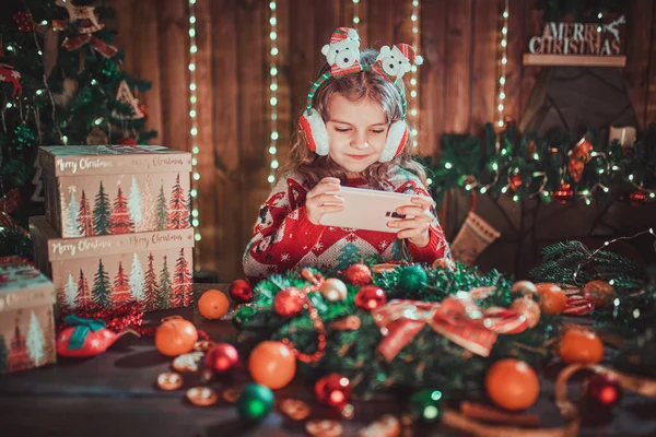 Дівчина використовує телефон біля ялинки в декоративному інтер'єрі. Різдво і Новий рік фото . — стокове фото