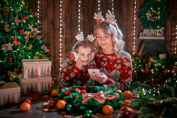 Мати і дочка дивляться телефон поруч з ялинкою і покупки онлайн — стокове фото